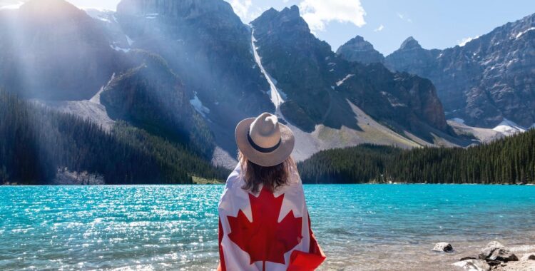 a woman in canada standing in front of a lake with a canada flag wrapped around her